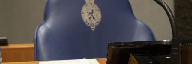 Voorzittersstoel met hiervoor de voorzittershamer, twee vellen papier en een microfoon.