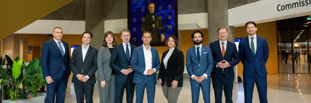 De leden van de commissie poseren in de Statenpassage in een rij naast elkaar voor het kunstwerk over de Grondwet. 