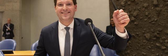 Thom van Campen zit op de stoel van de Voorzitter en houdt de Voorzittershamer vast.