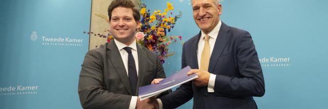 Thom van Campen (links) en Sybrand Buma staan naast elkaar, ze houden samen een document vast en schudden elkaar de hand. 