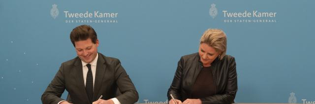 Kamervoorzitter Thom van Campen en informateur Rianne Letschert ondertekenen een document zittend aan een tafel.