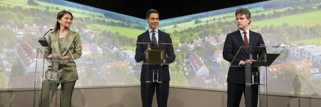 De drie fractievoorzitters achter drie katheders tegen een achterwand met luchtfoto van Nederland. Van links naar rechts Dilan Yeşilgöz (VVD), Rob Jetten (D66) en Henri Bontenbal (CDA). 