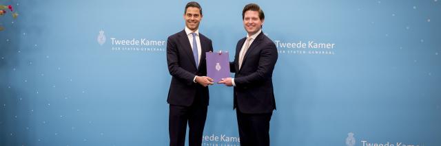 Voor een lichtblauwe achterwand staan formateur Jetten (links) en Kamervoorzitter Thom van Campen. Zij houden beiden het eindverslag vast. 