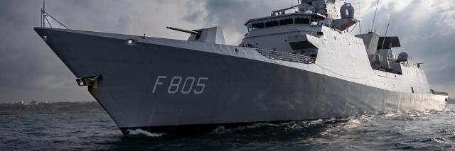 Fregat van voren gezien varend op zee, met wolken op de achtergrond. 