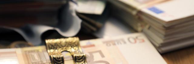 Verschillende stapeltjes bankbiljetten op een tafel van dichtbij gefotografeerd, de voorste heeft een geldklem.