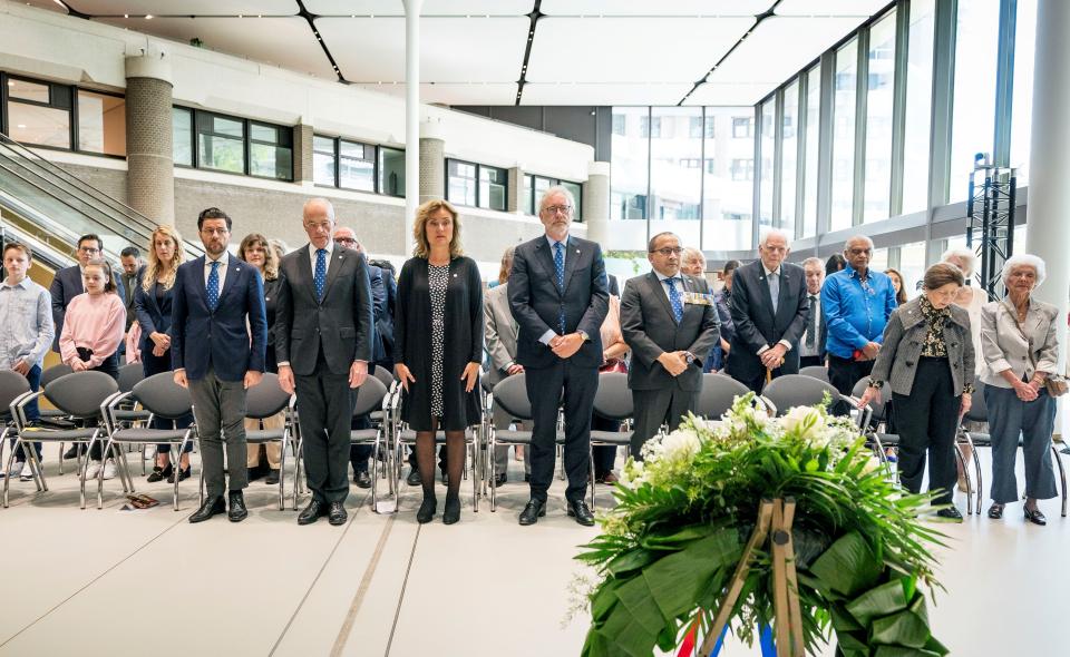 Op de voorgrond een krans, daarachter een rij personen die staand stilte in acht nemen.