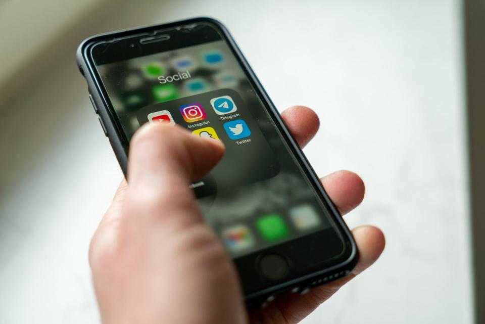 Beeld dichtbij van een linkerhand die een mobiele telefoon vasthoudt. Op het schermpje zijn de symbolen van de sociale media te zien.