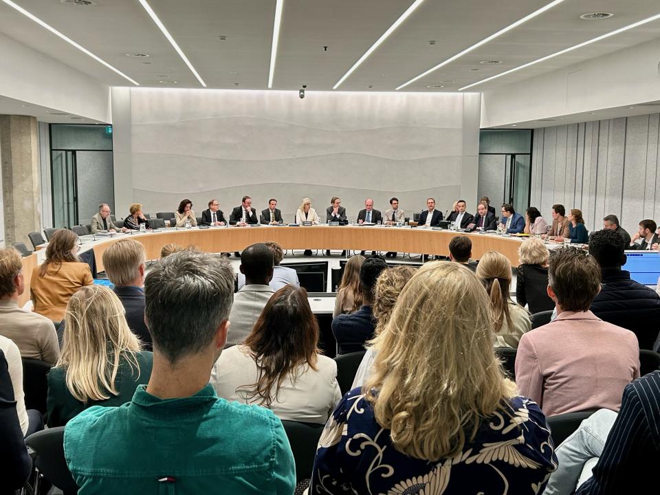 Beeld vanaf de publieke tribune in een commissiezaal: op de voorgrond de toeschouwers op de rug gezien, in de verte in een halve cirkel de Kamerleden van de commissie Financiën.