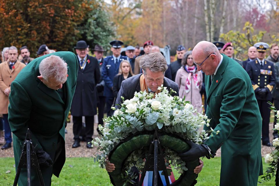 Een krans op een standaard van achteren gezien, ervoor Kamervoorzitter Martin Bosma en links en rechts twee heren in groen kostuum. Daarachter staand publiek in rijen opgesteld.