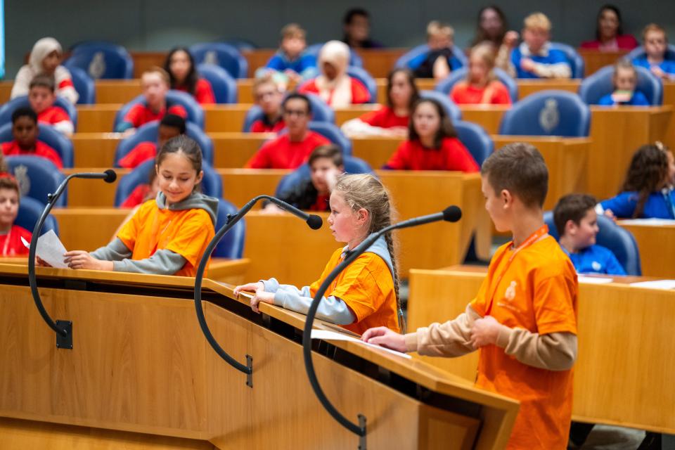 drie basisschoolleerlingen staan achter de interruptiemicrofoon