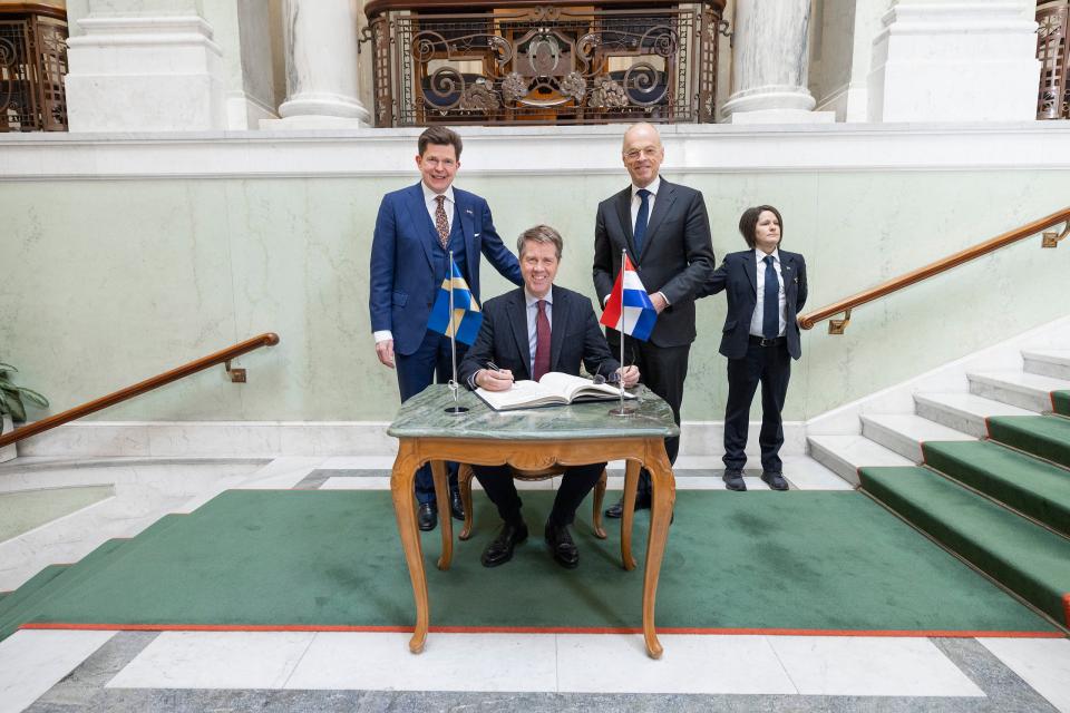 Achter een tafeltje in een trapportaal zit Kamervoorzitter Martin Bosma. Achter hem de Voorzitter van de Eerste Kamer en die van de Zweedse Rijksdag. Nog iets meer naar achteren een beveiliger. 
