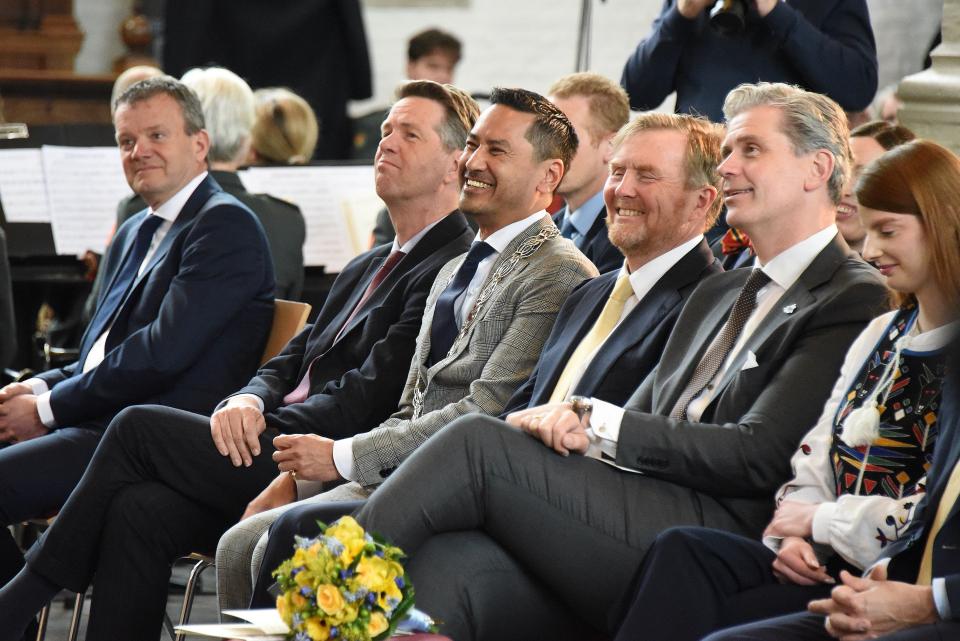 Op de voorste rij in een zaaltje zit een aantal mensen lachend naast elkaar in stoelen. Onder hen de Koning en Kamervoorzitter Martin Bosma.