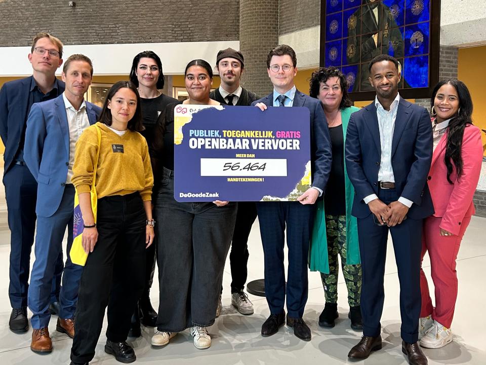 Groepsfoto in de Statenpassage. Op de foto staan de initiatiefnemers van DeGoedeZaak en de leden van de commissie voor de Verzoekschriften en de Burgerinitiatieven. Twee van hen houden een bord ivast, waarop staat: Publiek, toegankelijk, gratis openbaar vervoer. Meer dan 56.464 handtekeningen!