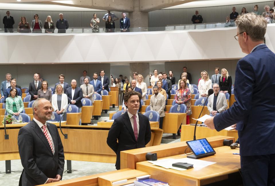 Kamerleden Ruud Verkuijlen (links) en Bram Kouwenhoven staan in de plenaire zaal van de Tweede Kamer. Op de voorgrond Kamervoorzitter Martin Bosma op de rug gezien. Op de achtergrond staan Kamerleden achter hun zetel.