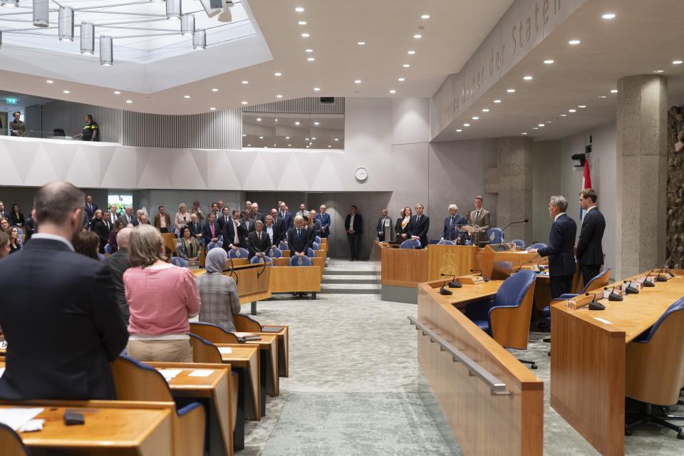 Tweede Kamerleden staan achter hun stoel in de plenaire zaal.