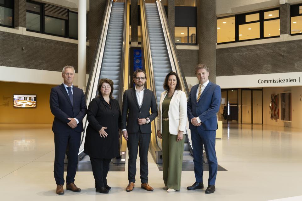 De leden van de parlementaire enquêtecommissie Corona staan voor de roltrappen in de Statenpassage.