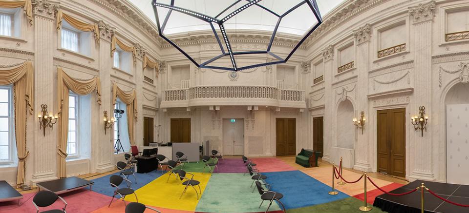 Panorama van de Oude Zaal, met gekleurd tapijt en stoelen.
