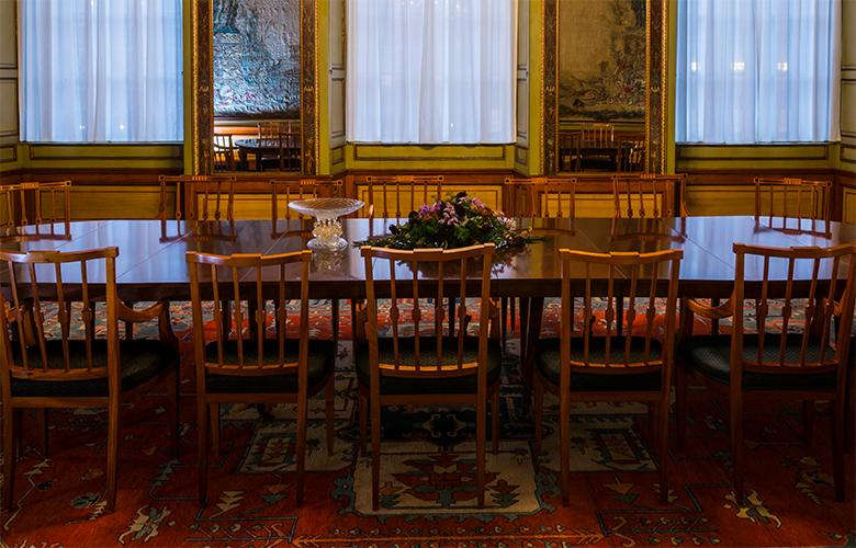 Lange houten tafel met aangeschoven stoelen, middenin de Stadhouderskamer.