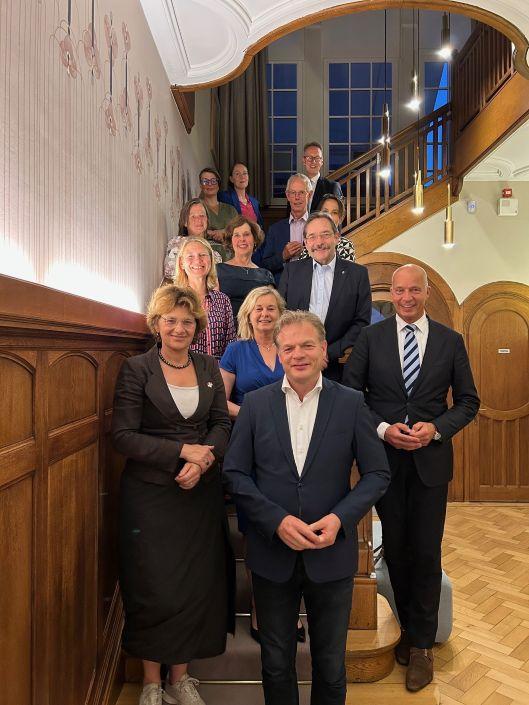 Tien kamerleden staan voor een trap.