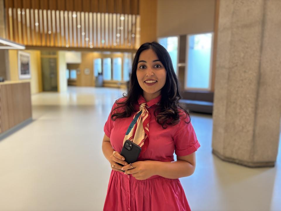 Sophia poseert in het Kamergebouw, achter haar een grote ruimte met betonnen pilaren en ramen aan de rechterzijde.