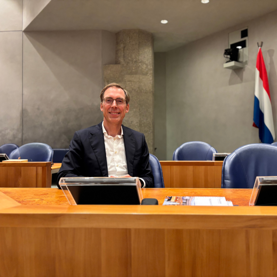 Sander Weeber in de plenaire zaal in het Voorzittersgestoelte. Rechts achter hem de Nederlandse vlag.