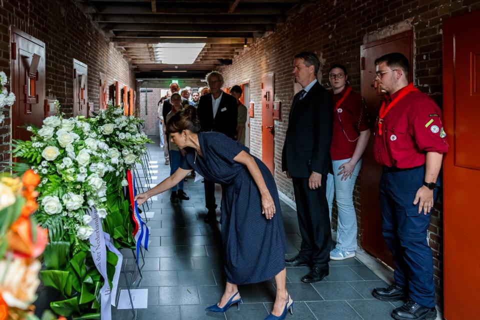 In een gang links enkele kransen op rekken, rechts Tweede Kamervoorzitter Martin Bosma en waarnemend Eerste Kamervoorzitter Mei Li Vos. Zij buigt zich voorover om nog iets aan de krans te schikken.