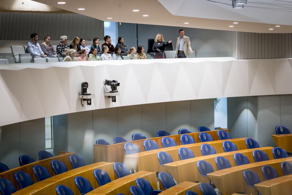 Een groep mensen staat op de publiekstribune van de plenaire zaal.