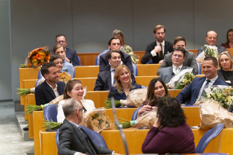 Beeld van een deel van de plenaire zaal met Kamerleden in de bankjes. Een aantal van hen heeft een bos bloemen voor zich liggen. 