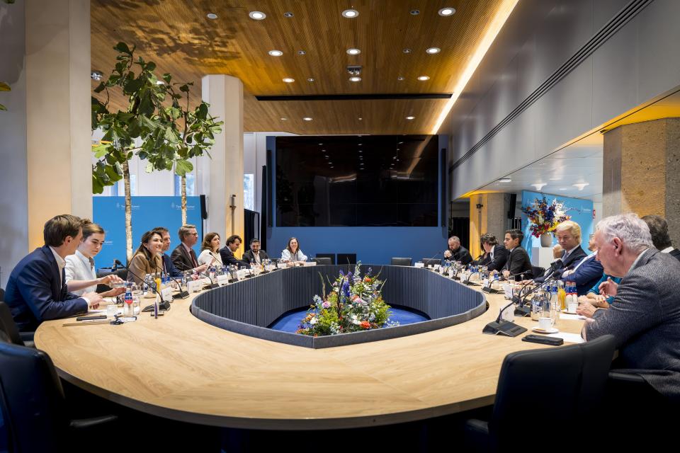 Rond de houten ovale tafel in de Max van der Stoelzaal zijn alle lijsttrekkers zichtbaar en Kamervoorzitter Martin Bosma.  