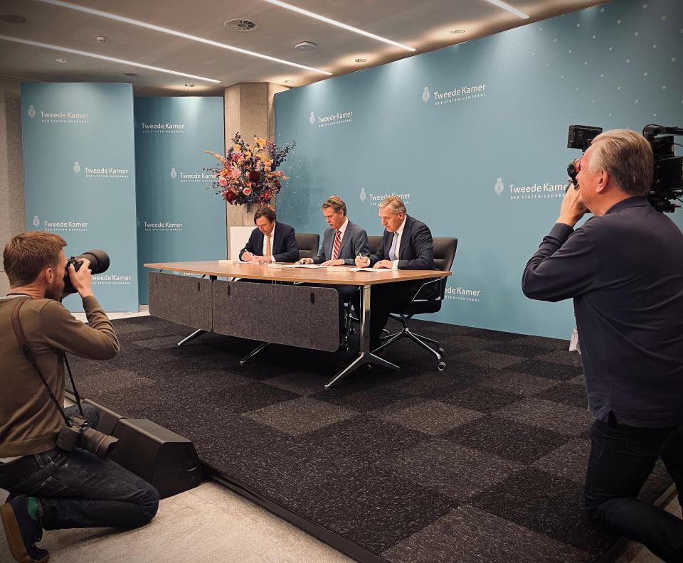 Kamervoorzitter Martin Bosma met aan weerszijden de informateurs Hans Wijers en Sybrand Buma achter een tafel. Op de voorgrond twee fotografen. 