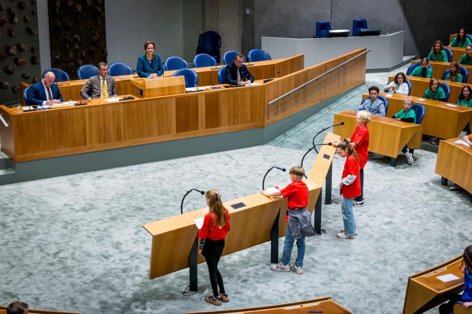 Vier kinderen staan achter de interruptiemicrofoons. In vak K zitten vier bewindspersonen.