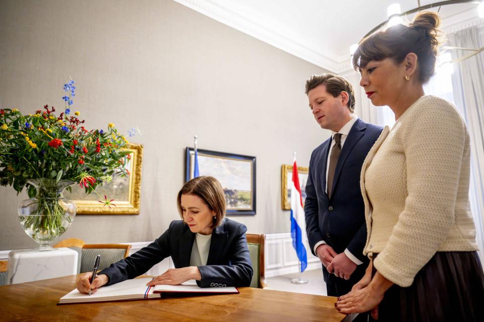 Maia Sandu zit aan een tafel en schrijft op een document. Hierachter staan Thom van Campen en Meil Vos, zij kijken toe.