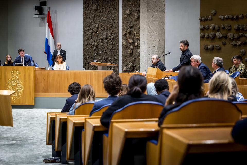 President Zelensky staat achter het katheder en spreekt het parlement toe in de plenaire zaal. Kamerleden zijn zichtbaar op de rug, Kamervoorzitters Thom van Campen en Mei Li Vos zitten op hun plek links op de foto. 