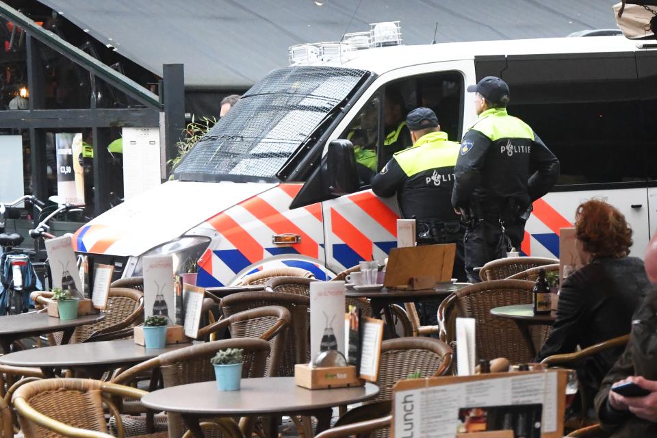 Twee politieagenten staan bij een politiebus, geparkeerd naast een terras.