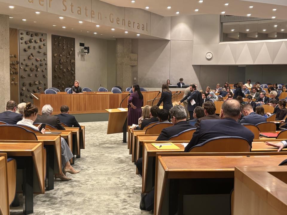 Plenaire vergaderzaal van de Tweede Kamer, de Kamerleden in de zetels zijn op de rug zichtbaar. Op de plek waar normaal gesproken de ministers zitten, vak K, zit nu informateur Rianne Letschert. 