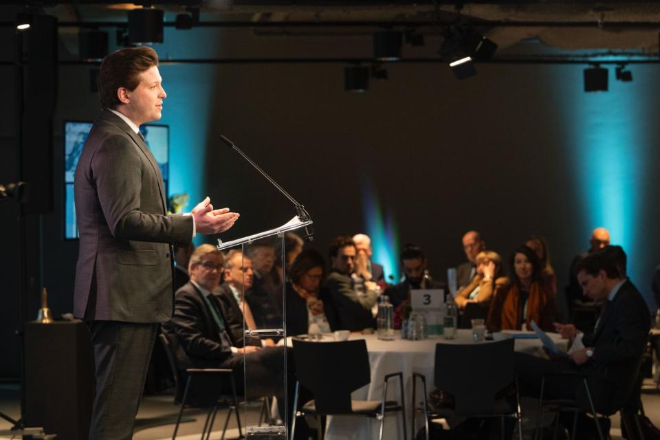 Thom van Campen is vanaf de zijkant gefotografeerd. Hij staat achter een spreekgestoelte.