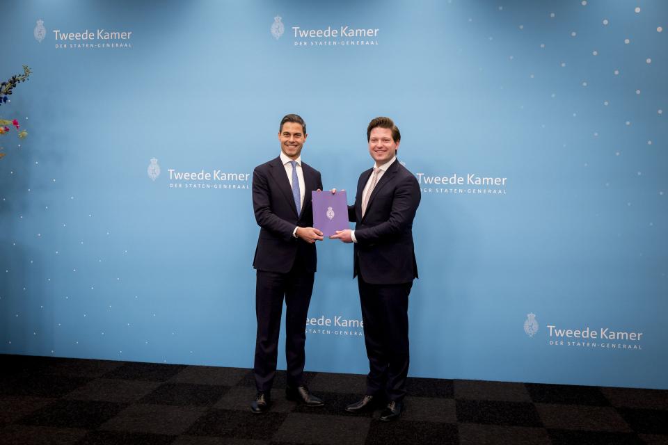 Voor een lichtblauwe achterwand staan formateur Jetten (links) en Kamervoorzitter Thom van Campen. Zij houden beiden het eindverslag vast. 