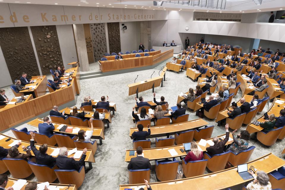 De plenaire zaal van de Tweede Kamer. De zaal is gevuld met Kamerleden. Een deel van hen steekt de hand op.