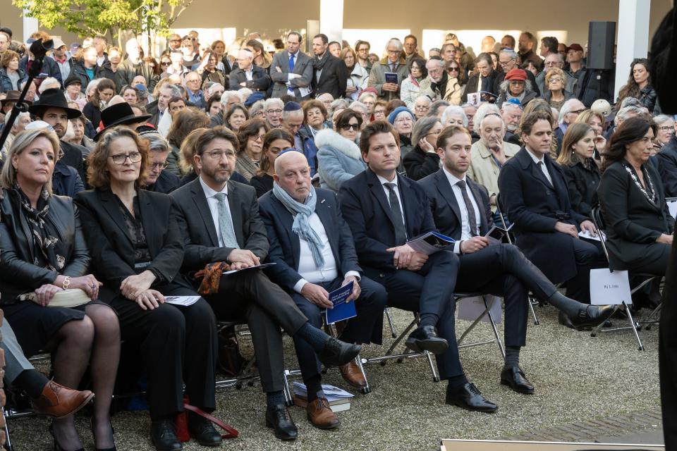 Mensen zitten op stoelen en luisteren aandachtig. Op de voorste rij zit Kamervoorzitter Thom van Campen.