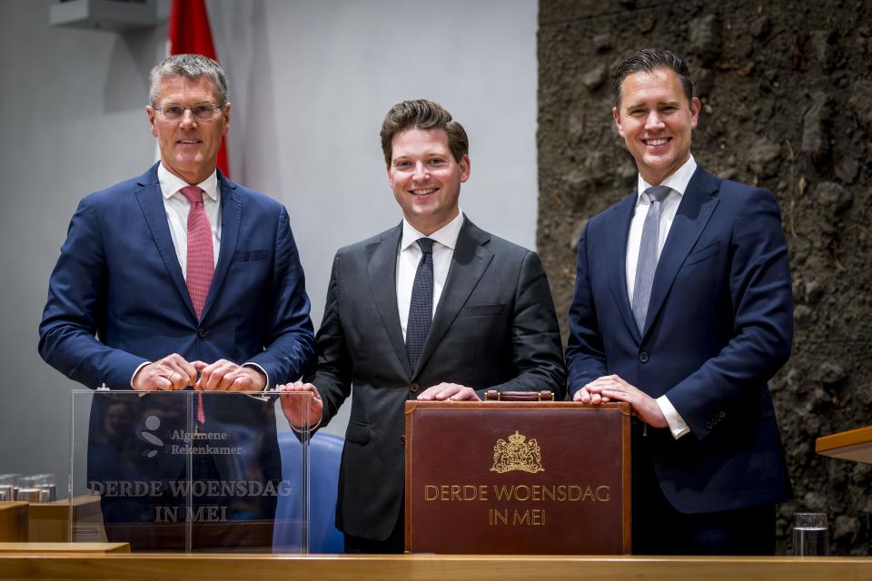 De president van de Algemene Rekenkamer Pieter Duisenberg (links), Tweede Kamervoorzitter Thom van Campen en minister Eelco Heinen van Financiën (rechts) staan in de plenaire zaal. Voor hen twee koffertjes met de tekst 'Derde woensdag in mei'. 