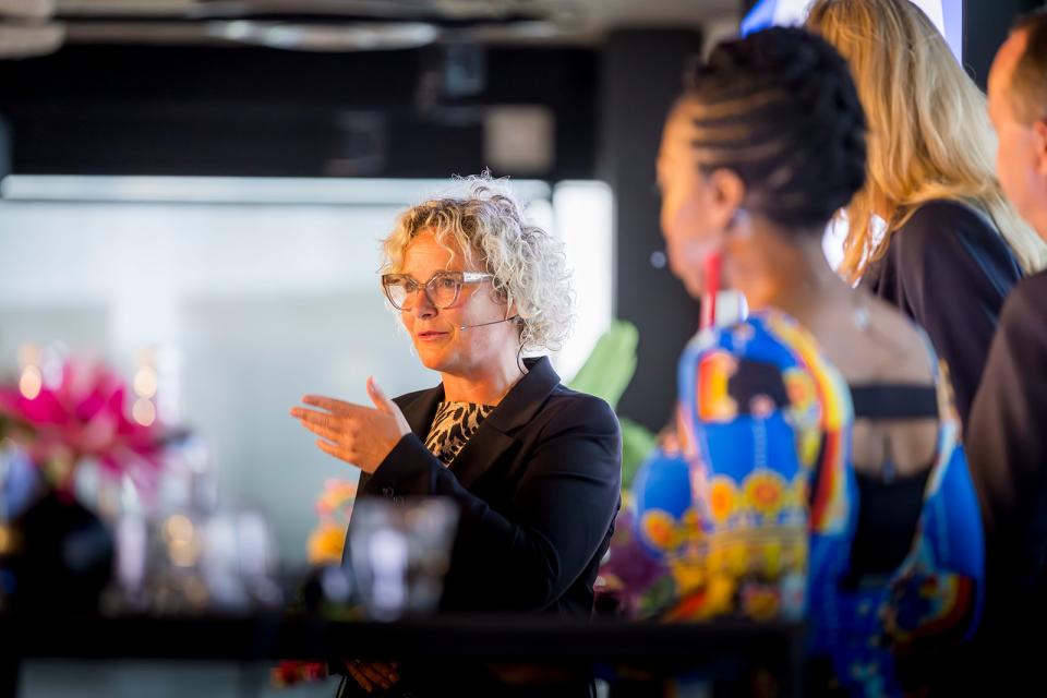 In het midden ondervoorzitter Wieke Paulusma, die schuin de zaal inkijkt. Rechts naast haar, aan de zijkant van het podium, drie mensen op de rug gezien. 