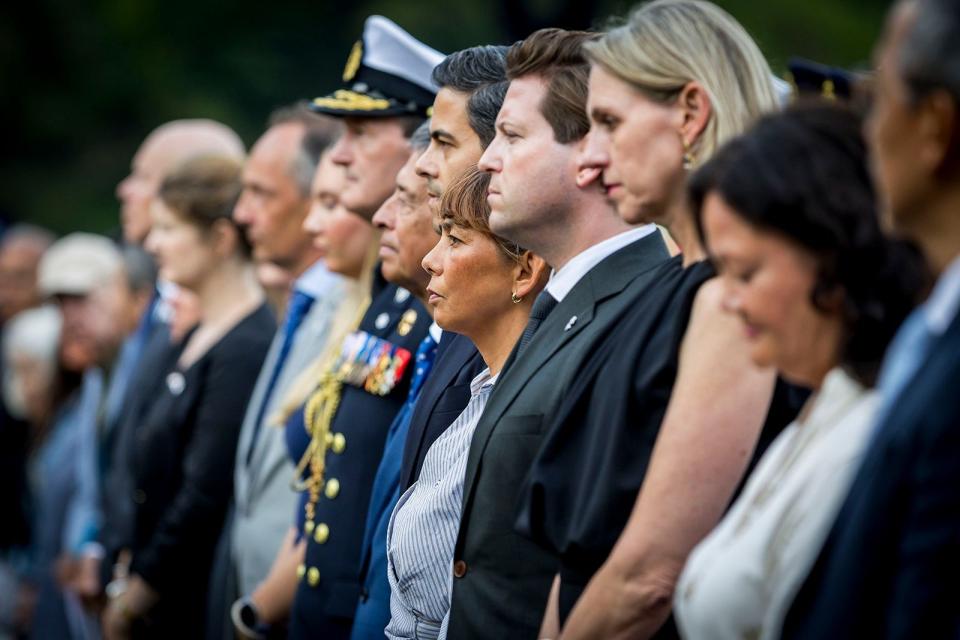 Kamervoorzitters Thom van Campen en Mei Li Vos staan op de eerste rij, tussen een groep andere genodigden, tijdens de herdenking op zaterdag 15 augustus 2026.