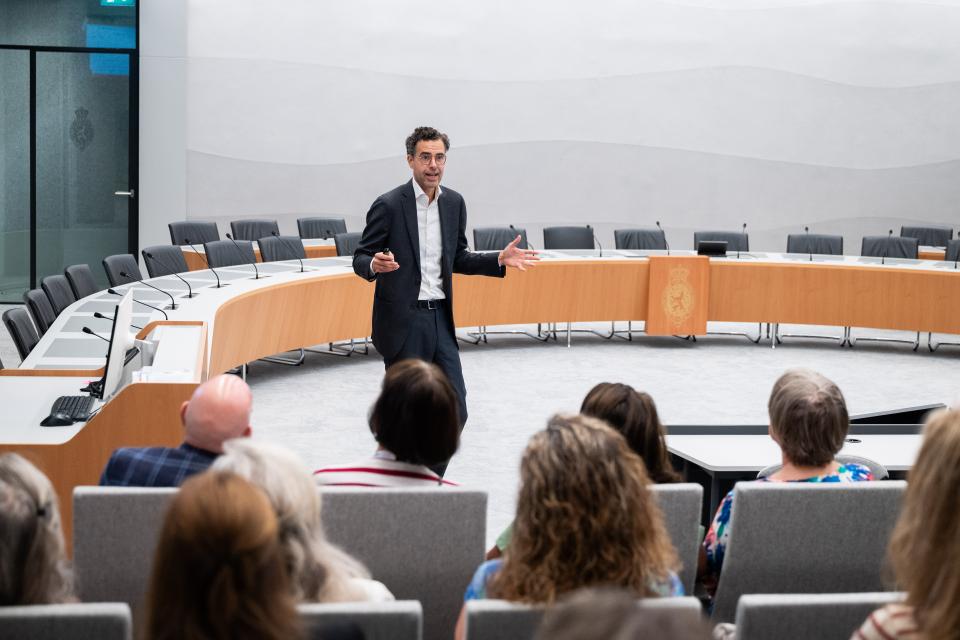 Hoogleraar Ronald Kroeze staat in een commissiezaal. Op de tribune zit publiek.