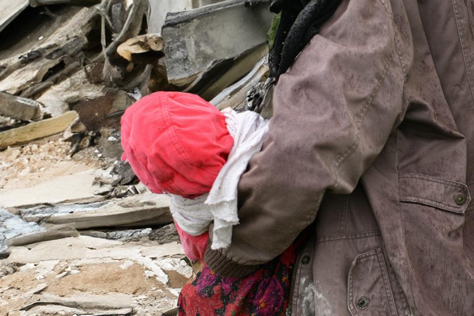 Een kind wordt gedragen door een ouder bij een gebombardeerd huis in Gaza. 