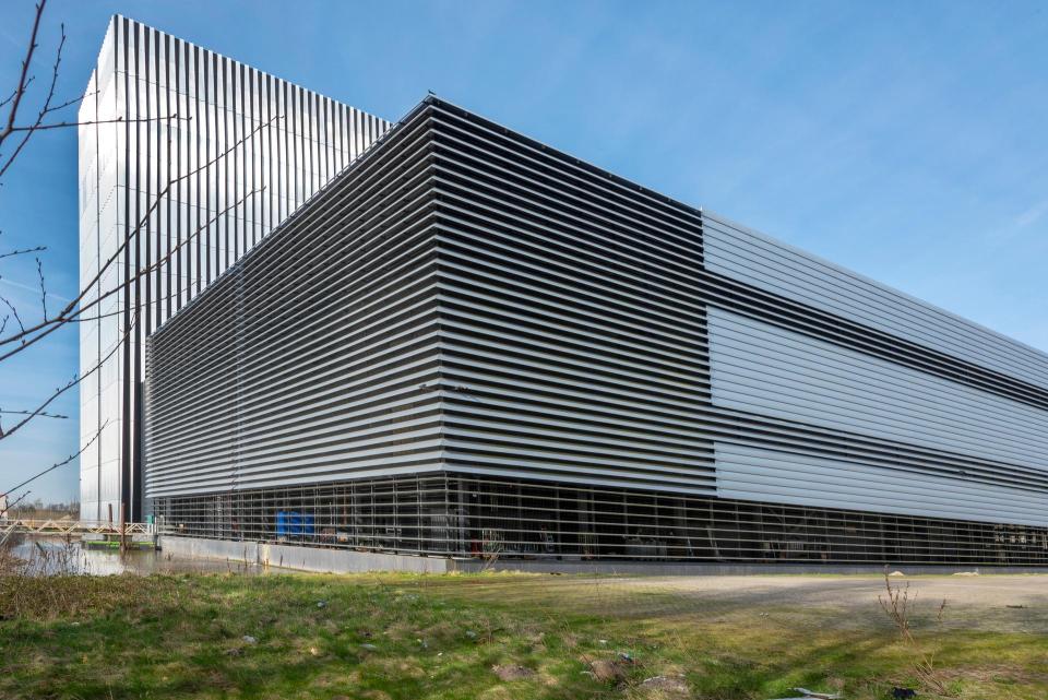 Buitenaanzicht van een datacenter in Amsterdam: op een grasveld is de rechterhoek van een strak grijs gebouw gefotografeerd.