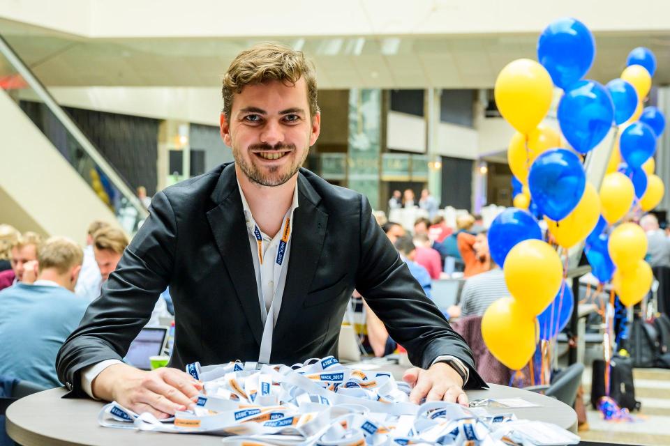 Tom staat bij een tafel met daarop keycords van de hackathon om uit te delen aan deelnemers