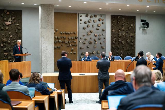 Geert Wilders staat achter het spreekgestoelte in de plenaire zaal. Op de voorgrond Kamerleden van op de rug gezien. In vak K zitten vier kabinetsleden, waaronder minister-president Dick Schoof.