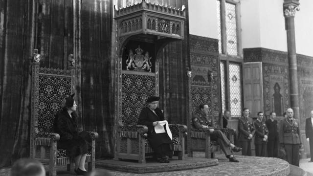 Koningin Wilhelmina zit in de troon, rechts van haar prinses Juliana, links prins Bernhard. 