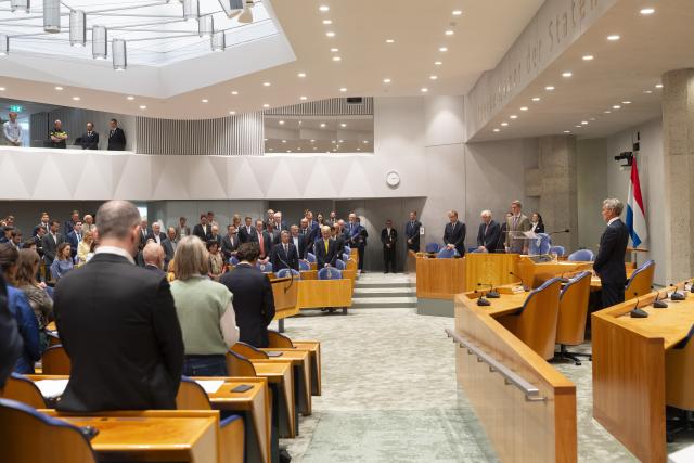 Tweede Kamerleden staan achter hun stoel in de plenaire zaal.