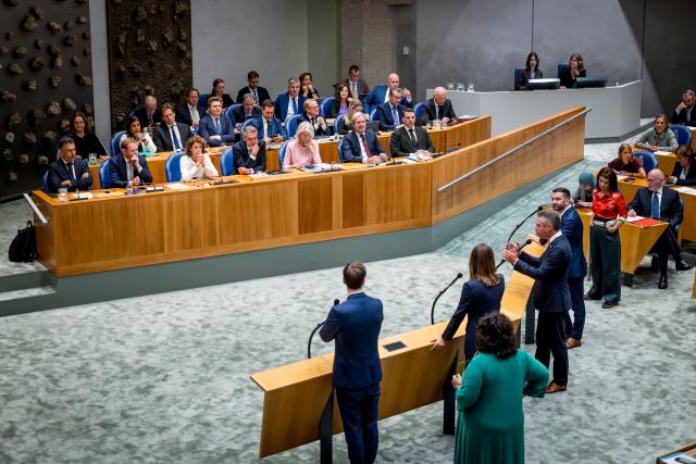 Meerdere fractievoorzitters staan bij de vier interruptiemicrofoons. In vak K zitten alle bewindslieden.